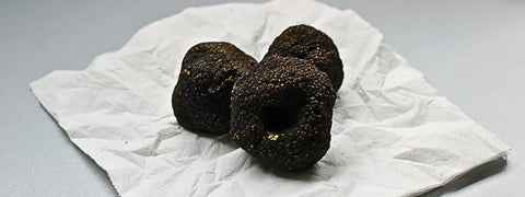 Three black truffles displayed on a rustic wooden surface in a storage guide article