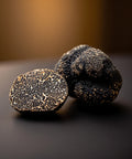Two black truffles on a dark surface with a blurred background