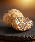 Two truffles on a dark surface with a blurred warm background